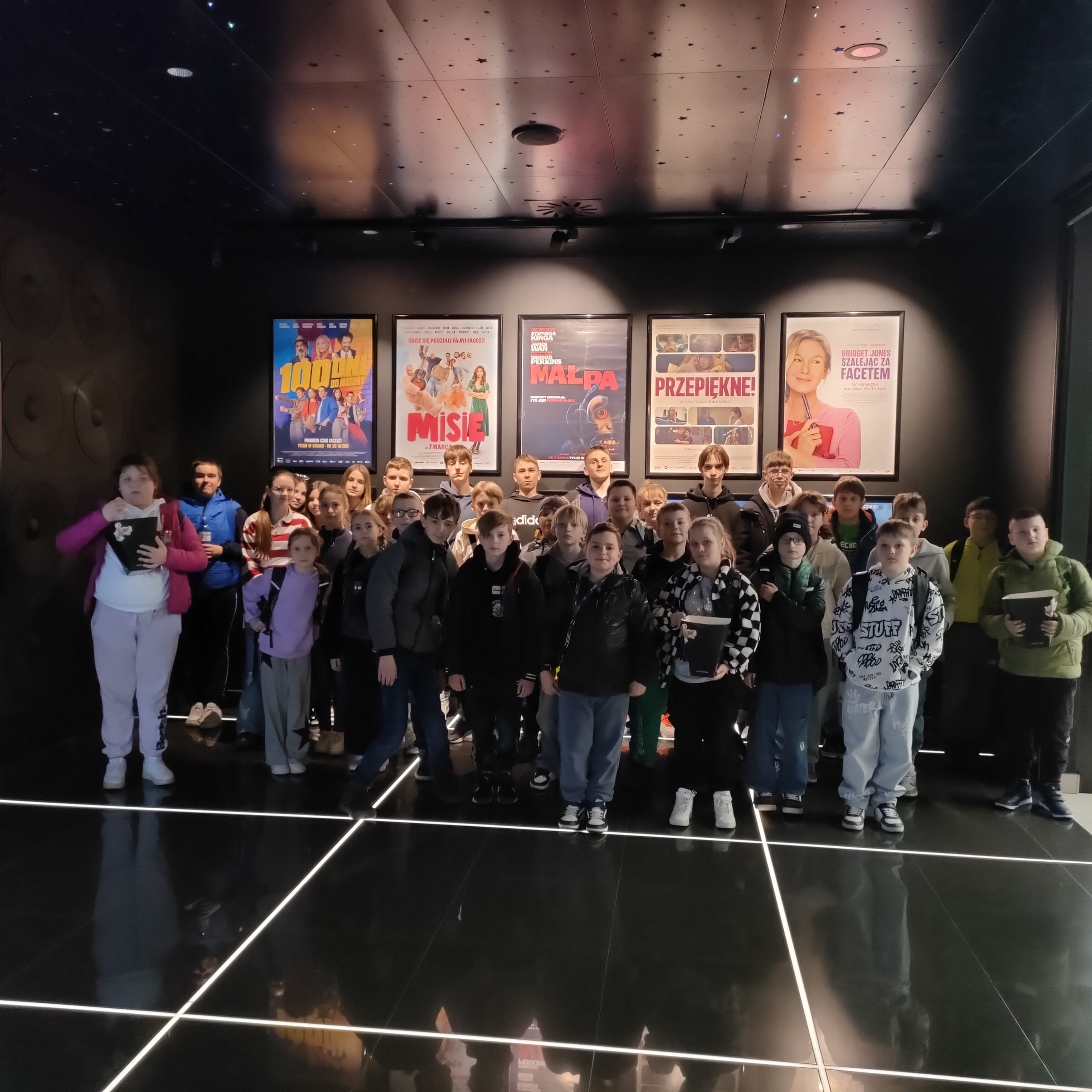 Grupa uczniów stojąca przy wejściu do kina. W tle widać plakaty z tytułami filmów