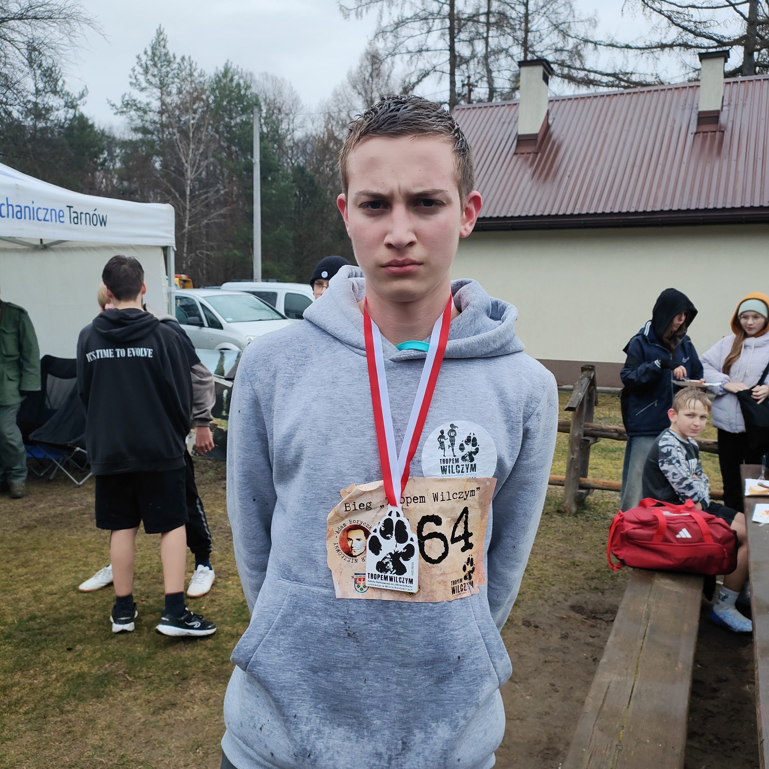 Chłopiec ubrany na sportowy, zawieszonym na szyi medalem i przyklejonym do bluzy numerem, który odznaczał się podczas biegu