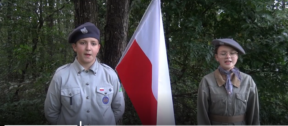 Chłopiec i dziewczynka stojący koło flagi polskiej śpiewający piosenki żołnierskie